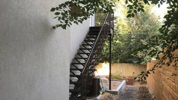 Eine Betontreppe führt zu einer Holzterrasse, umgeben von einem Garten mit Mulch und einem Holzzaun.