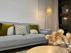 Un salon moderne avec un canapé gris, des coussins à motifs, un lampadaire en fibres tressées et un vase rempli de fleurs.