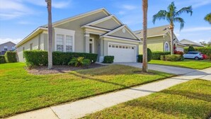 A single-story house with a garage, surrounded by well-maintained lawns and palm trees. - South Facing Pool & Spa- 2 Master Bedrooms (Clermont)