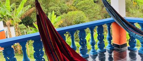 Una hamaca en un balcón con vistas a vegetación exuberante y suelo de baldosas.
