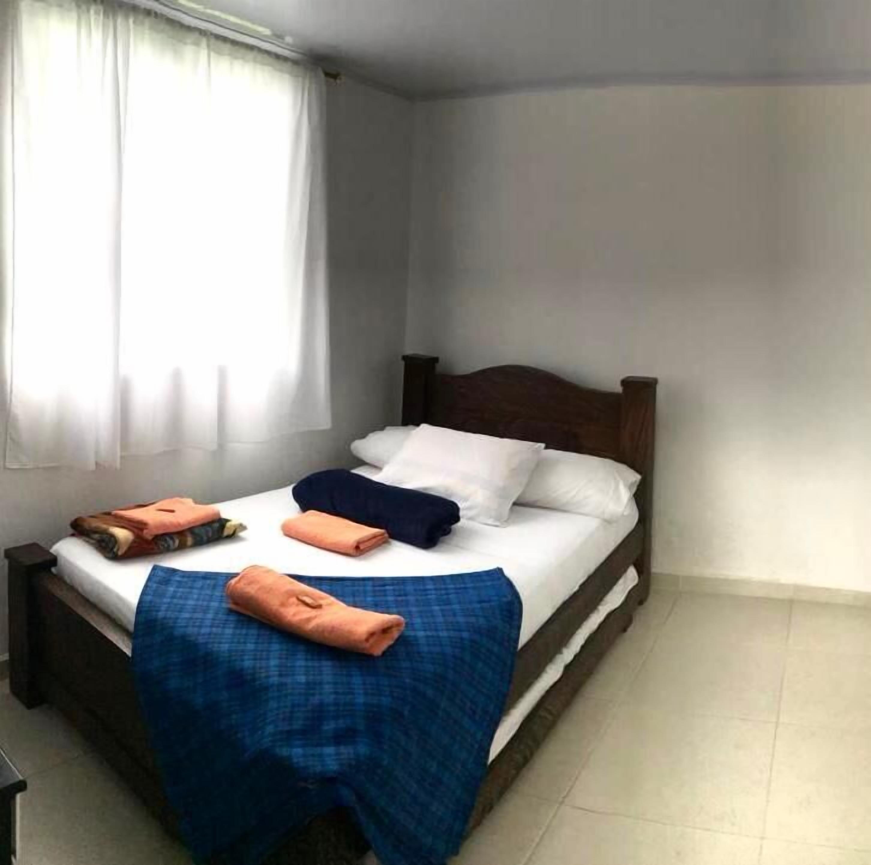 A single bed with a wooden headboard, white bedding, and a blue checkered blanket.