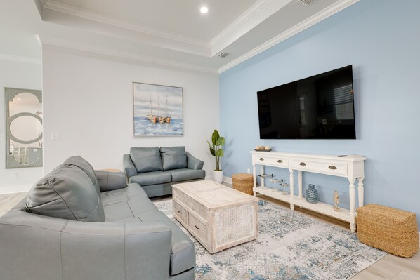 Una sala de estar con un sofá seccional gris, una consola blanca y un televisor de pantalla plana grande montado en la pared.