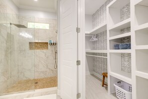 Un baño moderno con ducha de vidrio, paredes cubiertas de azulejos blancos y un mueble de almacenamiento empotrado con zócalos estampados.