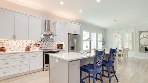 A modern kitchen with white cabinets, a stainless steel refrigerator, and a central island with blue bar stools. - Bright Foley Home w/ Patio - 7 Mi to Wharf & Beach (Foley)