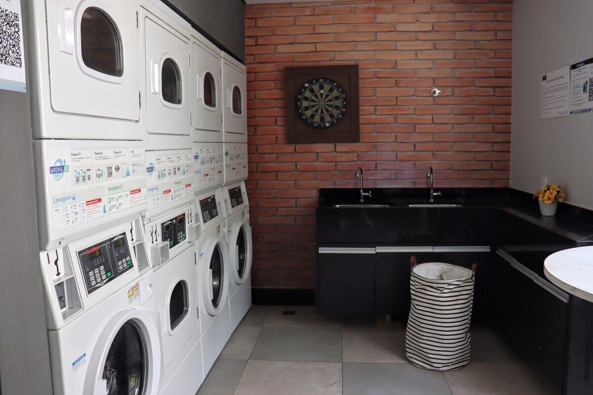Un área de lavandería con varias lavadoras, un dardo, un lavabo y un cubo de basura.