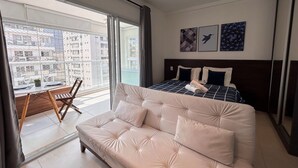Ett modernt hotellrum med en stor säng, en soffa, en balkong med en matplats och konstverk på väggen.