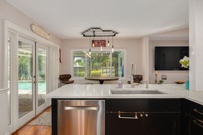 A modern kitchen with a large island, stainless steel appliances, and a view of a pool through glass doors.