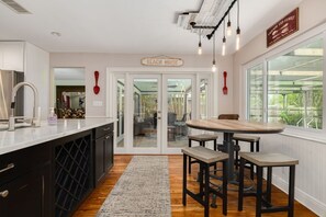 A kitchen with a dining area, a sign reading 'BEACH HOUSE', and a view through glass doors.