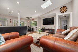A spacious living room with leather sofas, a coffee table, and a TV.