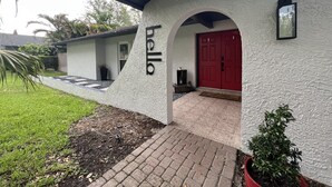 Una casa moderna con un cartel que dice 'hello', una puerta roja y un pequeño jardín.