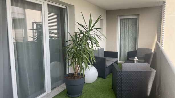 Un balcone con una pianta in vaso, mobili in vimini grigio e un tavolino con una lanterna.