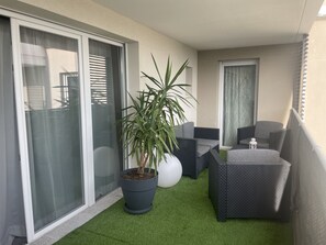 A balcony with a potted plant, grey wicker furniture, and a small table with a lantern.