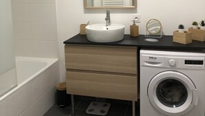 Un bagno moderno con lavandino bianco, uno specchio, una lavatrice e una vasca da bagno.