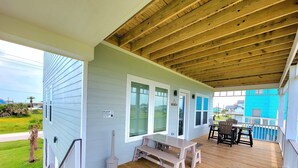 A covered porch with a wooden deck, a bench, and a table with chairs.
