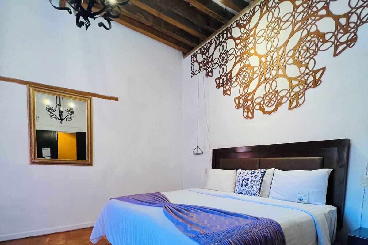 Ein Schlafzimmer mit einem Bett, einer Kristallleuchtre, einem Wandspiegel und einem dekorativen Wandbild.