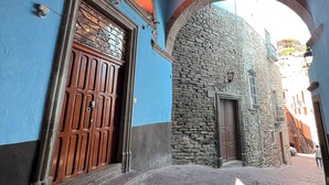Une rue étroite avec un immeuble bleu, un mur de pierre et une porte en bois.