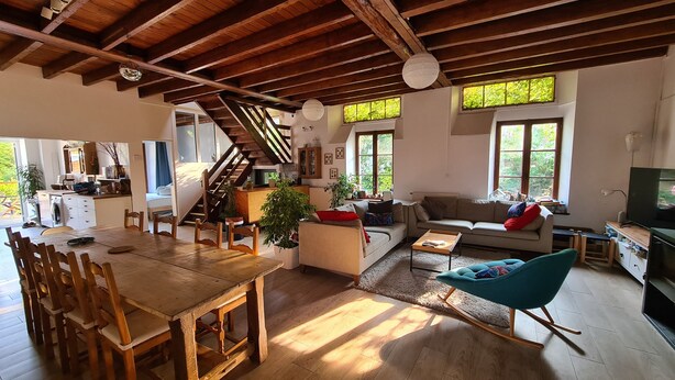 Een ruime woonkamer met een houten eettafel, een bank, een schommelstoel en een televisie.