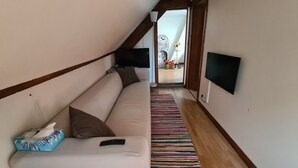Een smalle gang met een bank, een kleurrijk gestreept tapijt en een aan de muur bevestigde televisie.