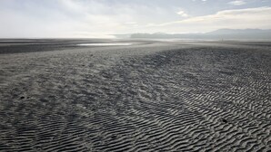 Una playa con una amplia extensión de arena y una vista distante de montañas bajo un cielo despejado.