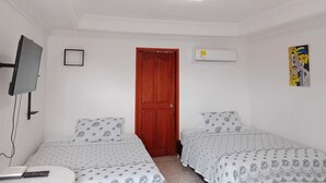 A room with two beds, a TV mounted on the wall, a door, and an air conditioning unit. - Habitacion Extragrande Cerca al Parque Venezuela (Barranquilla)
