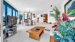 A modern living room with a flat-screen TV, wooden coffee table, and various plants. - Stunning High-Floor Unit with Spectacular Ocean, Diamond Head, and Waikiki Views (Honolulu)