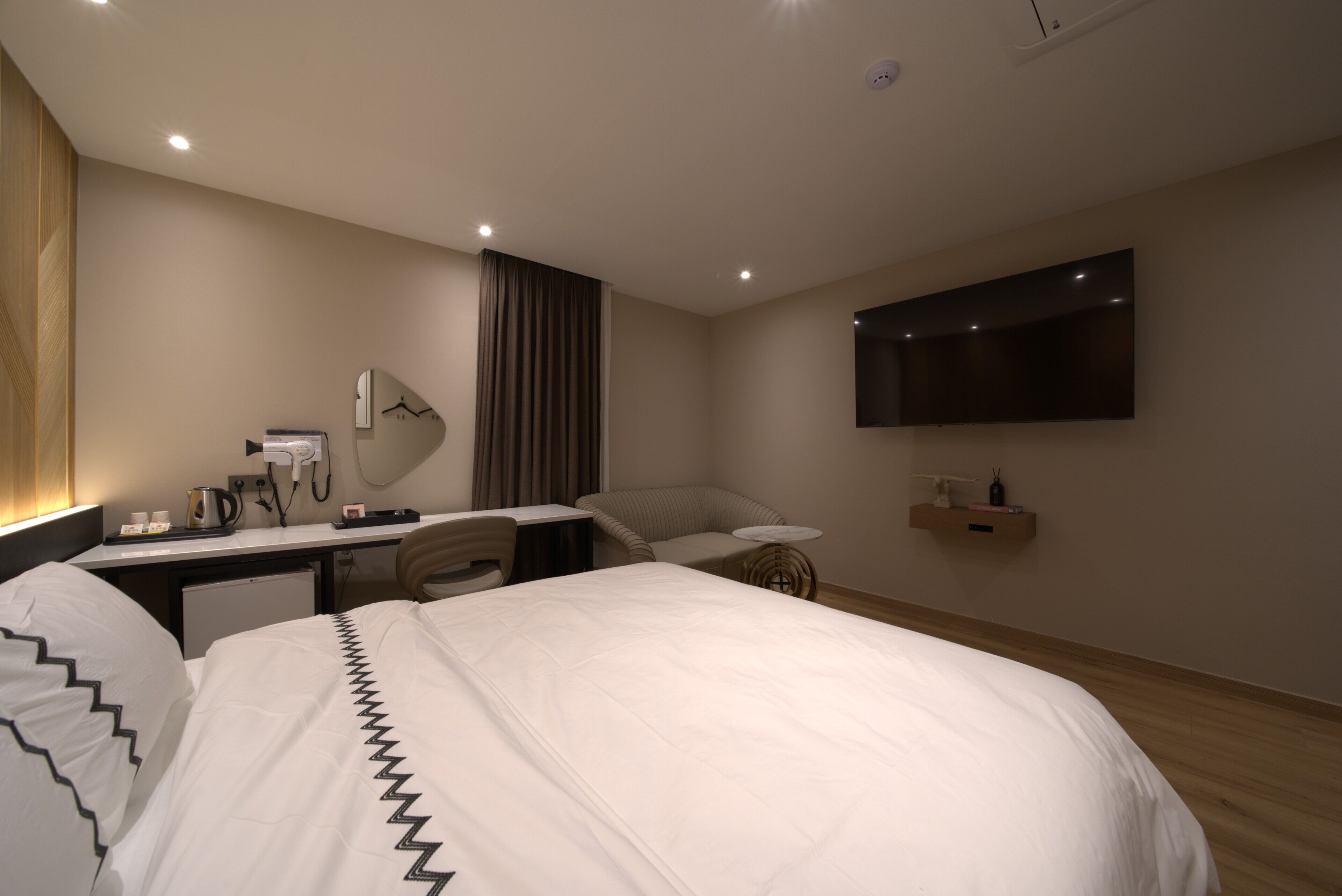 Una habitación de hotel moderna con una cama grande, un escritorio con espejo, un televisor de pantalla plana y una mesita.