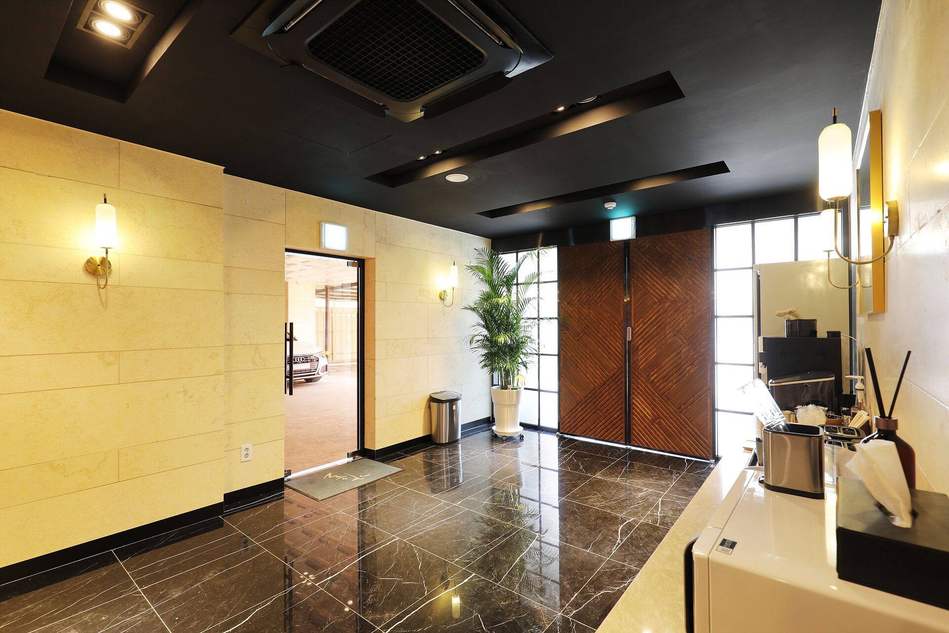 A modern lobby with a reception desk, a potted plant, and a large window.