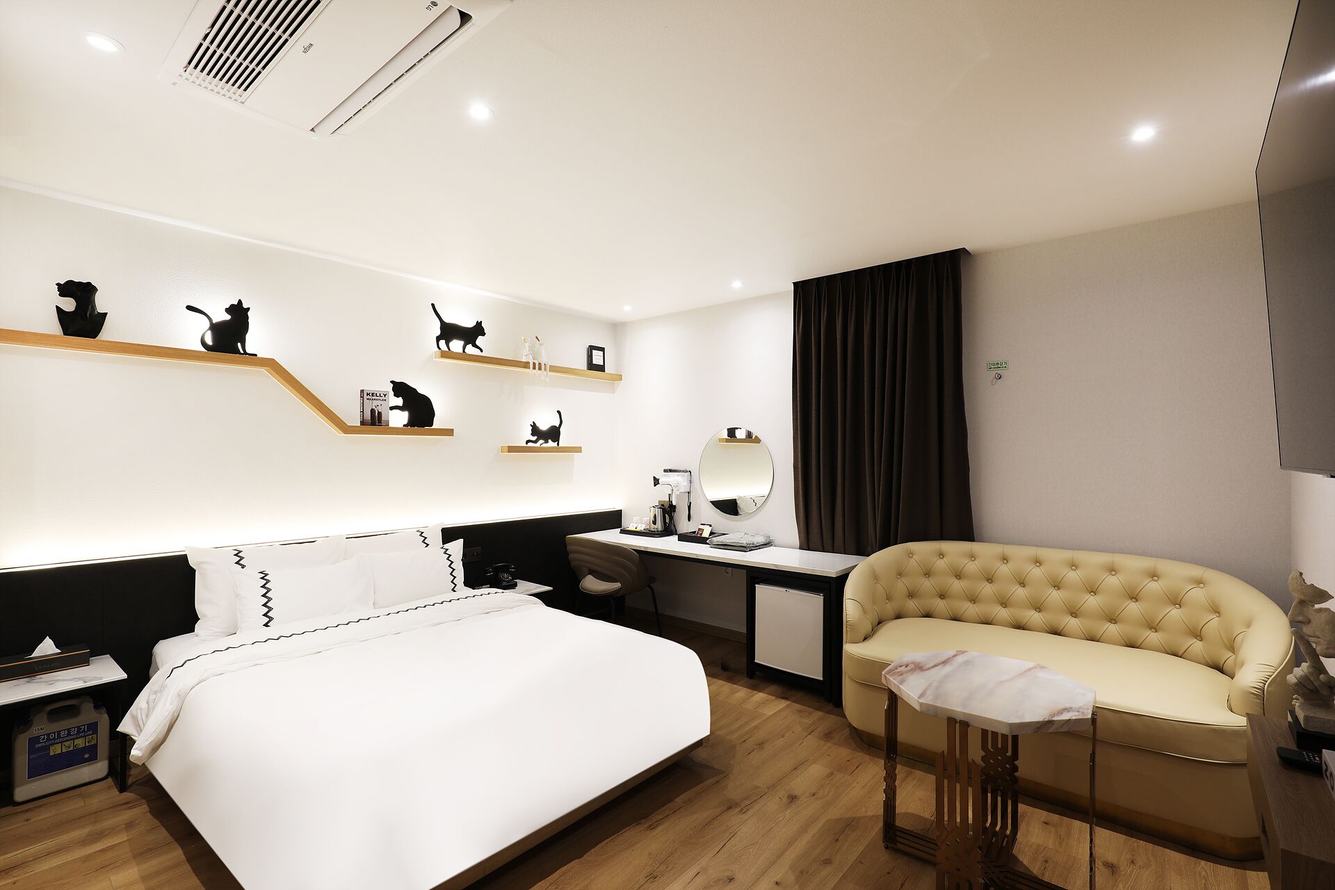 Una habitación de hotel moderna con una cama, un escritorio, un sofá y un estante de pared con siluetas de gatos.