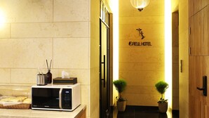 L’entrée d’un hôtel présente un design moderne, avec un comptoir d’accueil, une horloge numérique et deux plantes en pot.