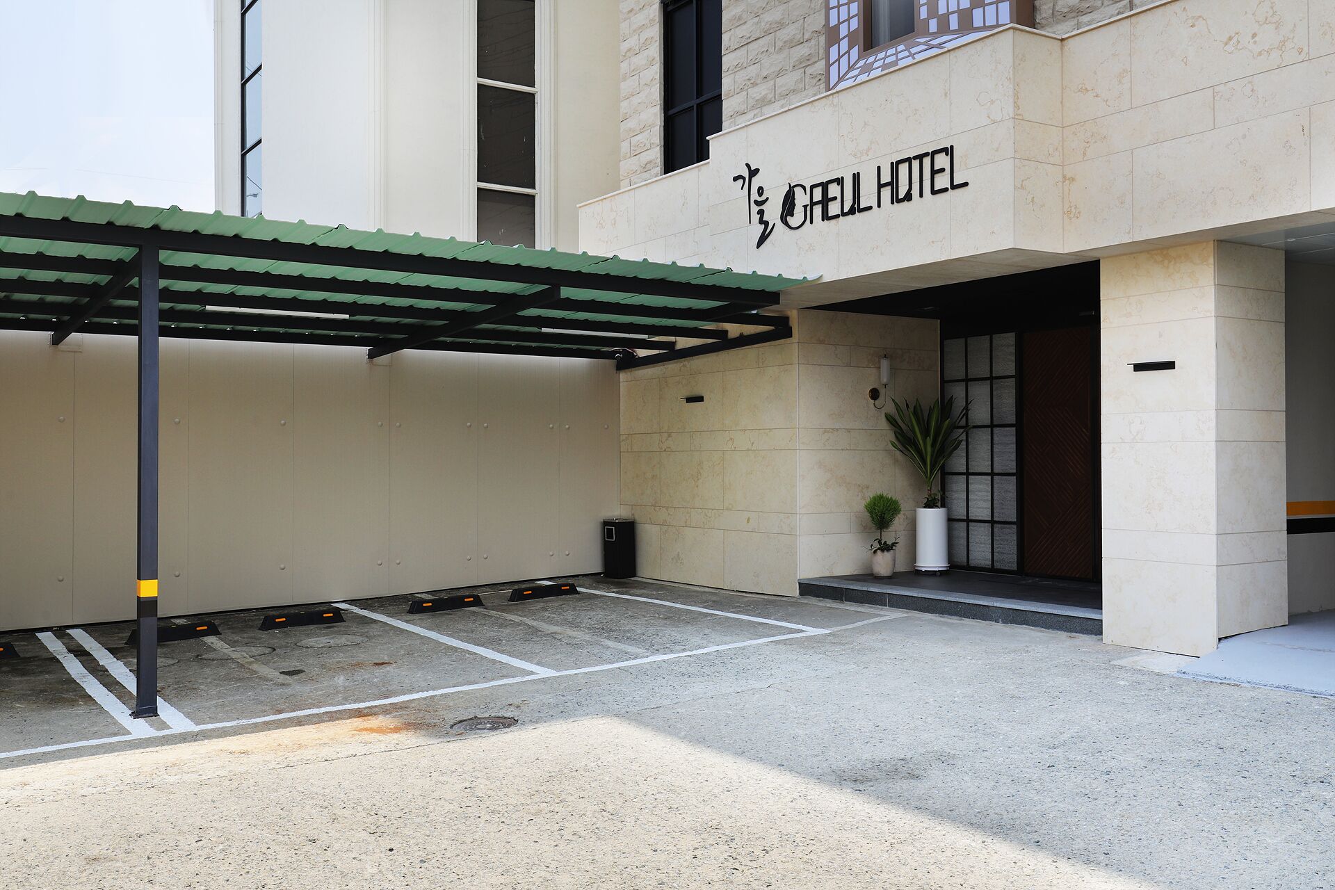 L’entrée d’un hôtel, avec un espace de stationnement couvert, un pot de fleurs et une enseigne indiquant « HÔTEL GAEL ».