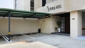 L’entrée d’un hôtel, avec un espace de stationnement couvert, un pot de fleurs et une enseigne indiquant « HÔTEL GAEL ».