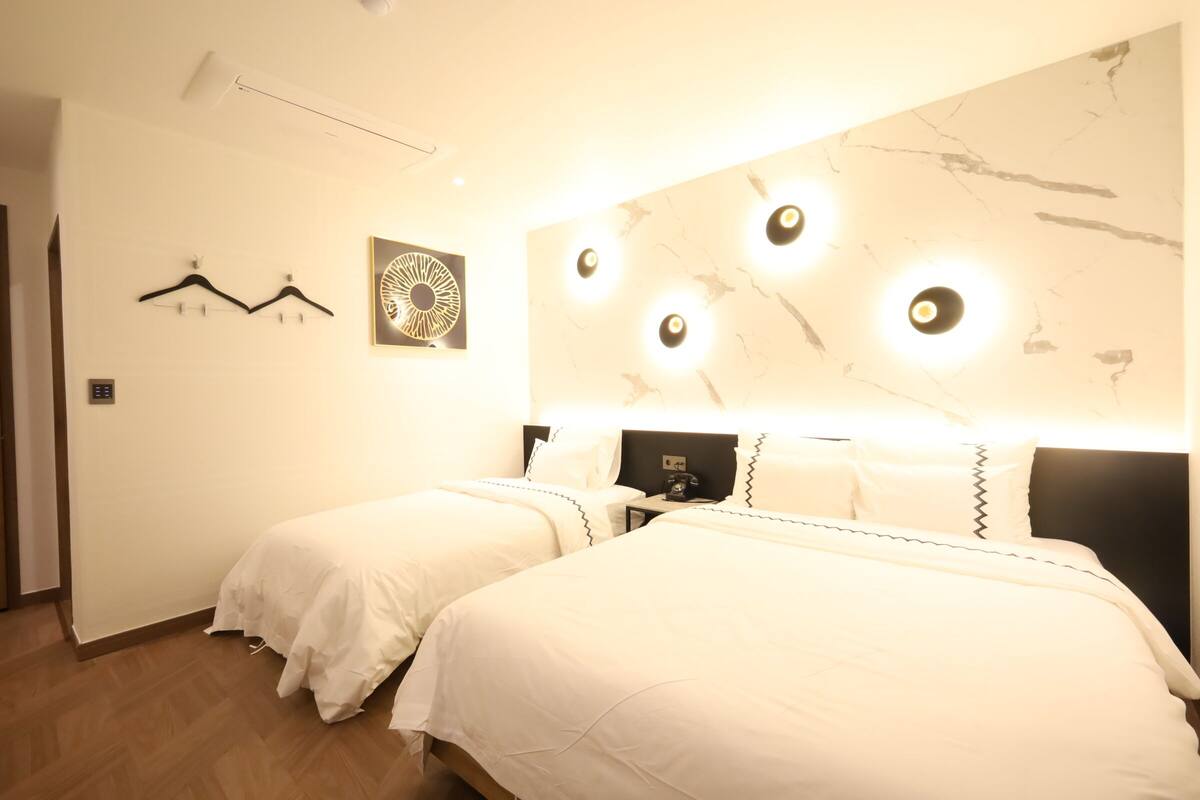 A hotel room with two beds, a wall-mounted light fixture, and a coat rack.
