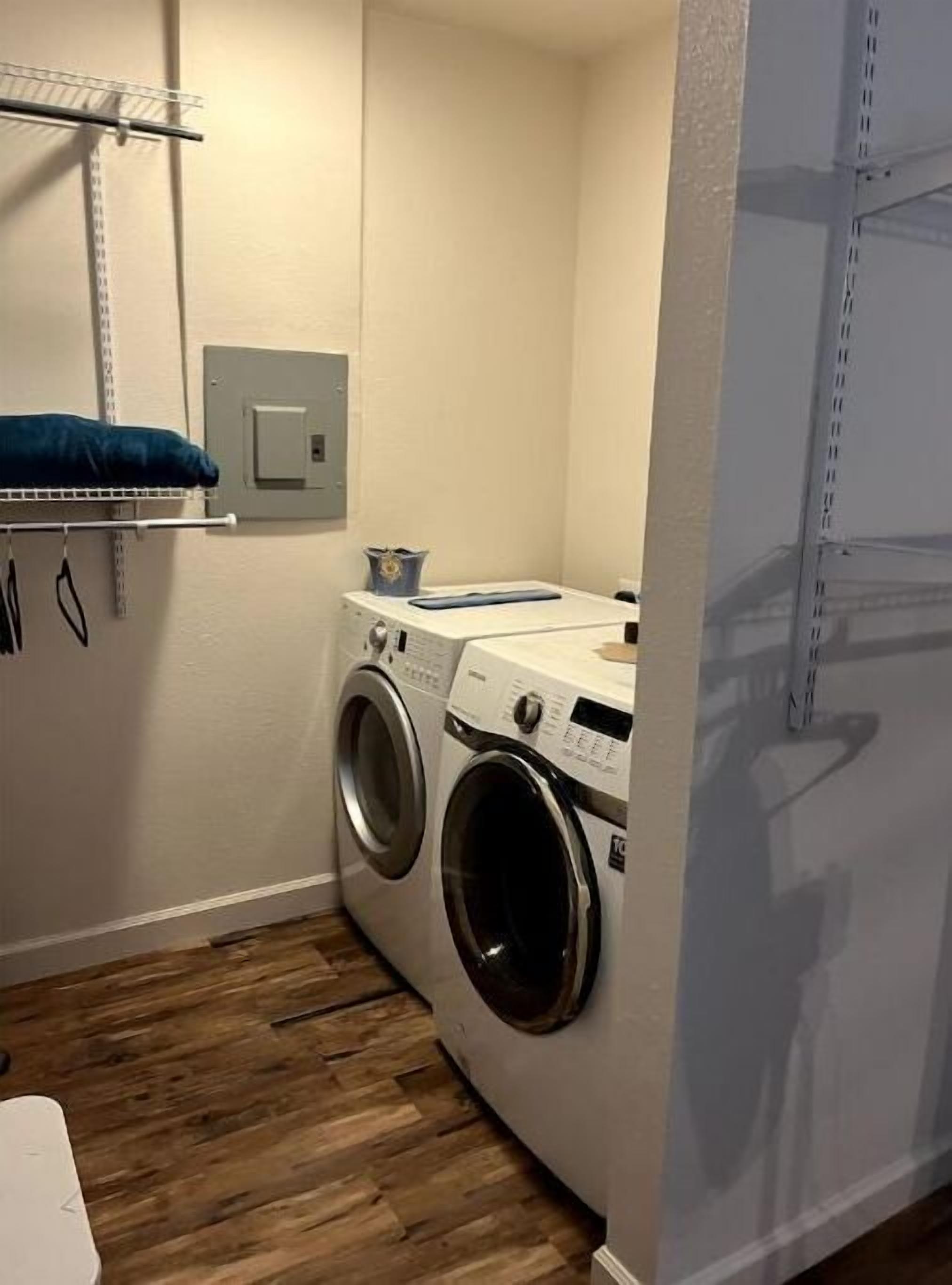Une buanderie équipée d’un lave-linge et d’un sèche-linge, une étagère avec une serviette bleue et une prise électrique au mur.