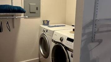 Une buanderie équipée d’un lave-linge et d’un sèche-linge, une étagère avec une serviette bleue et une prise électrique au mur.
