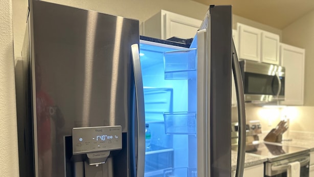 Un refrigerador de acero inoxidable con dispensador de agua, un microondas y una encimera de cocina al fondo.