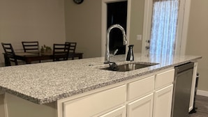 Una cocina con encimera de granito, armarios blancos y lavavajillas.