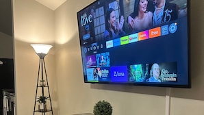 Una sala de estar con un televisor de pantalla plana montado en la pared, mostrando diferentes servicios de streaming.