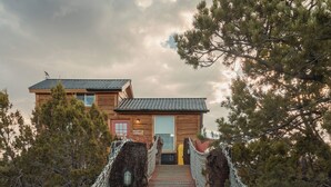 Un pont en bois menant à un chalet doté d’un toit en métal, entouré d’arbres.