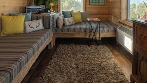 L’intérieur chaleureux d’un chalet avec un plafond en bois, un ventilateur de plafond, un canapé, une petite table et un radiateur.