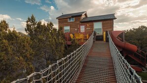 Une cabane en bois reliée à un toboggan par un pont de corde.