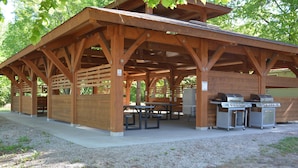 Un área de picnic cubierta con bancos y mesas de madera, y una parrilla para barbacoa.