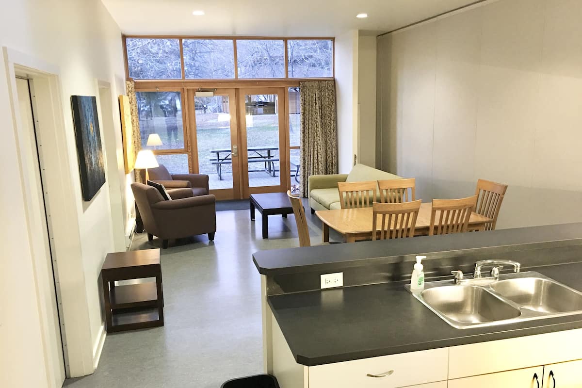 A compact kitchen with a dining area, a sofa, and a view through large windows.