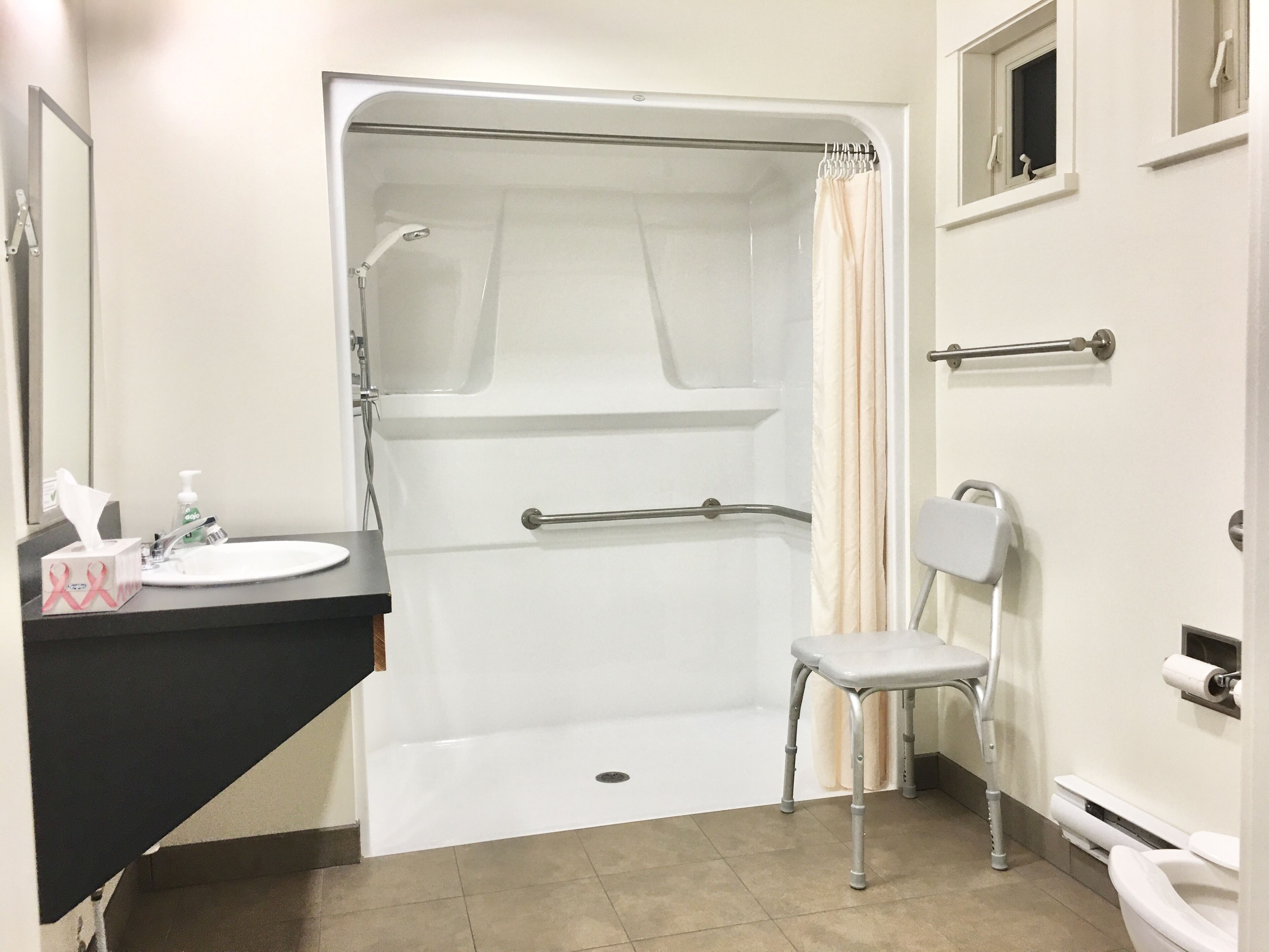 A bathroom with a shower, a sink, a toilet, and a chair.