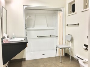 A bathroom with a shower, a sink, a toilet, and a chair. - Naramata Centre (Naramata)