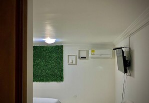 Une pièce avec un mur vert, un luminaire au plafond, un climatiseur fixé au mur et un téléviseur mural.