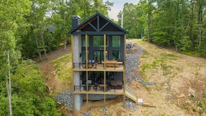 A two-story modern house with a balcony, surrounded by trees. - Juniper Ridge - Mountain Luxury | River & Golf Views | Outdoor Living and Hot Tub (Blue Ridge)
