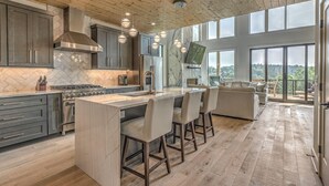 A modern kitchen with a central island, stainless steel appliances, and a large window overlooking a scenic view. - Juniper Ridge - Mountain Luxury | River & Golf Views | Outdoor Living and Hot Tub (Blue Ridge)