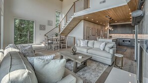 A spacious living area with a large sofa set, a coffee table, and a staircase leading to an upper level. - Juniper Ridge - Mountain Luxury | River & Golf Views | Outdoor Living and Hot Tub (Blue Ridge)