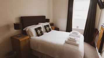 A neatly made bed with white linens and a striped headboard, a bedside lamp, and a small wooden nightstand with a lamp.
