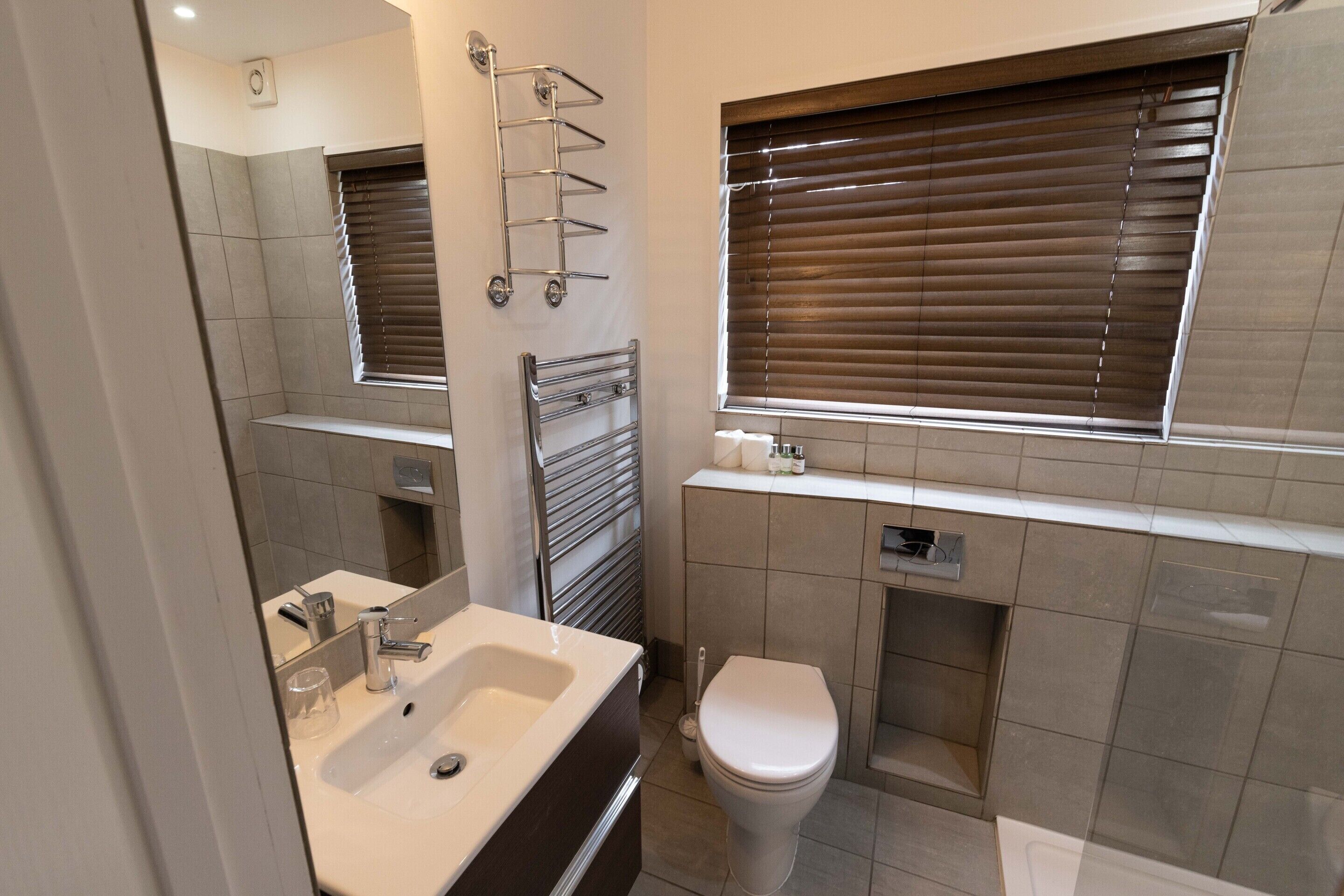 Un baño moderno con lavamanos, espejo, inodoro y persianas.